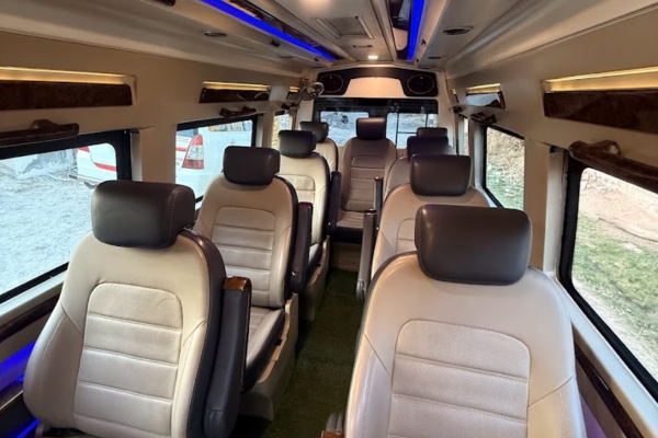 Luxury Tempo Traveller interior with comfortable leather seats, wide windows, and ambient blue lighting.